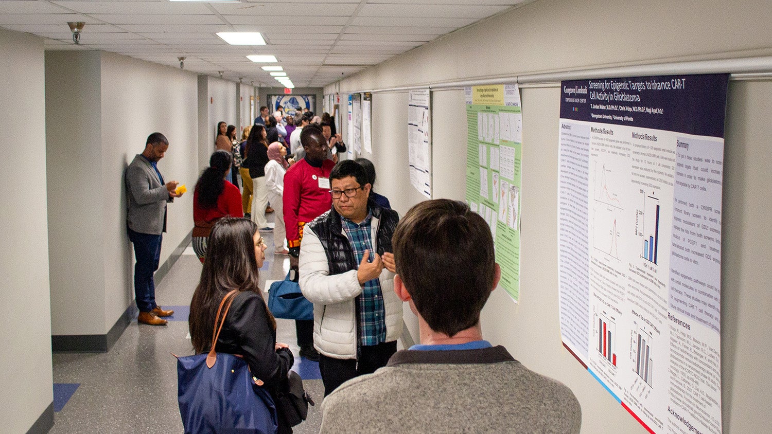 Symposium attendees discuss research in Pre-Clinical Hallway C during poster presentations.