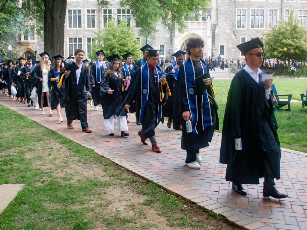 Graduates process across Copley Lawn at Commencement