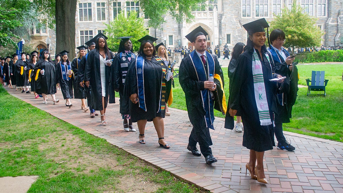 Students in graduation regalia process across Copley Lawn during Commencement