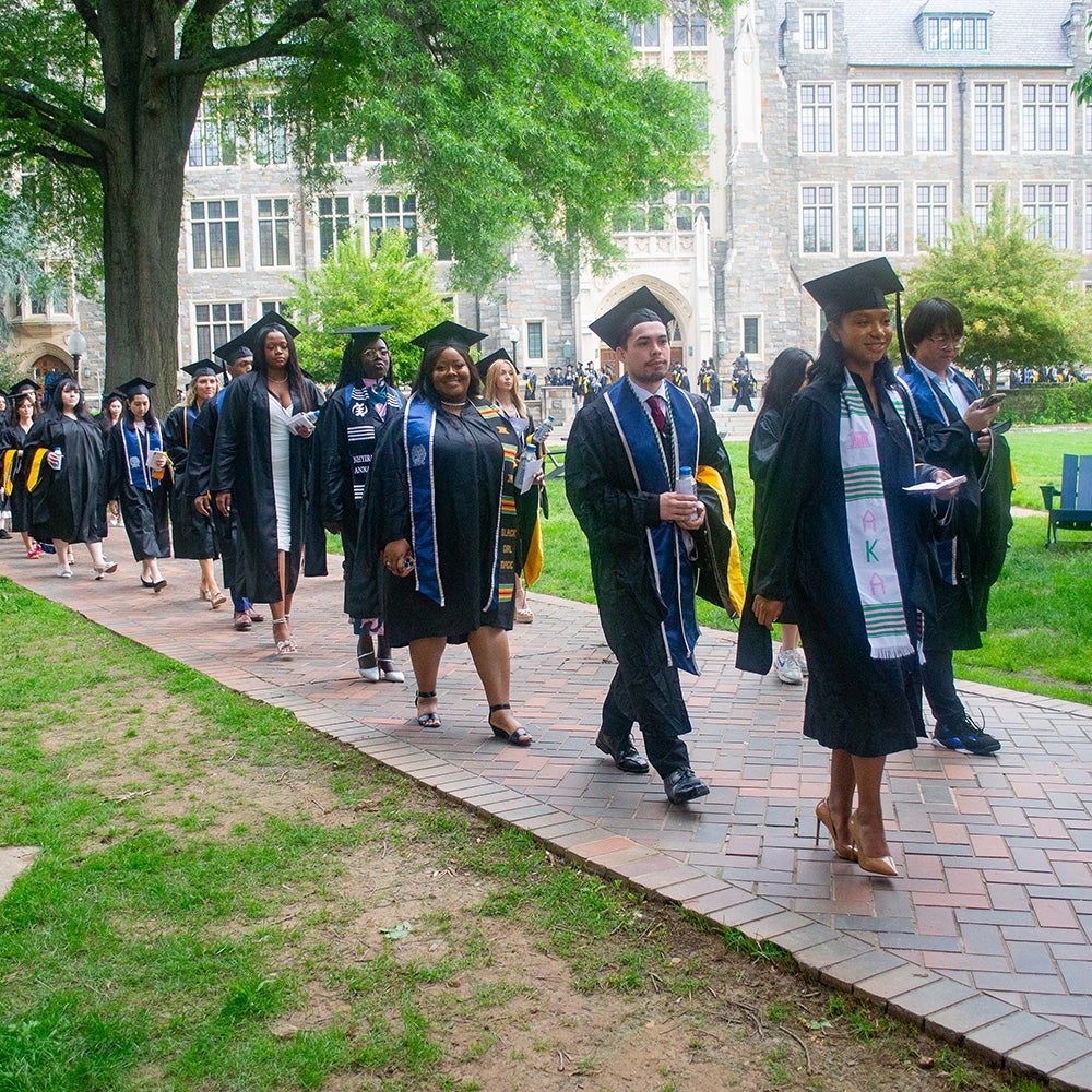 Students in graduation regalia process across Copley Lawn during Commencement