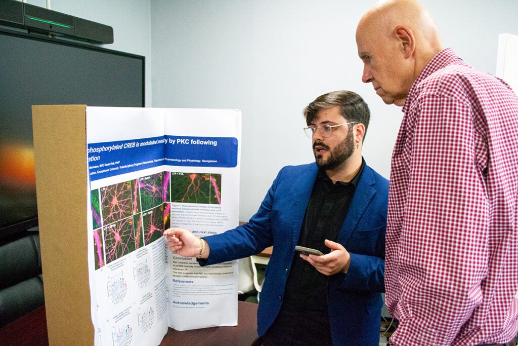 Stefano Vicini listens to a student poster presenter in May 2025