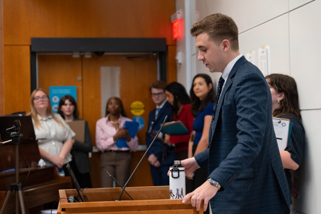 Side profile of Curtis Hoffmann standing at a podium and talking with members of the research team in the background