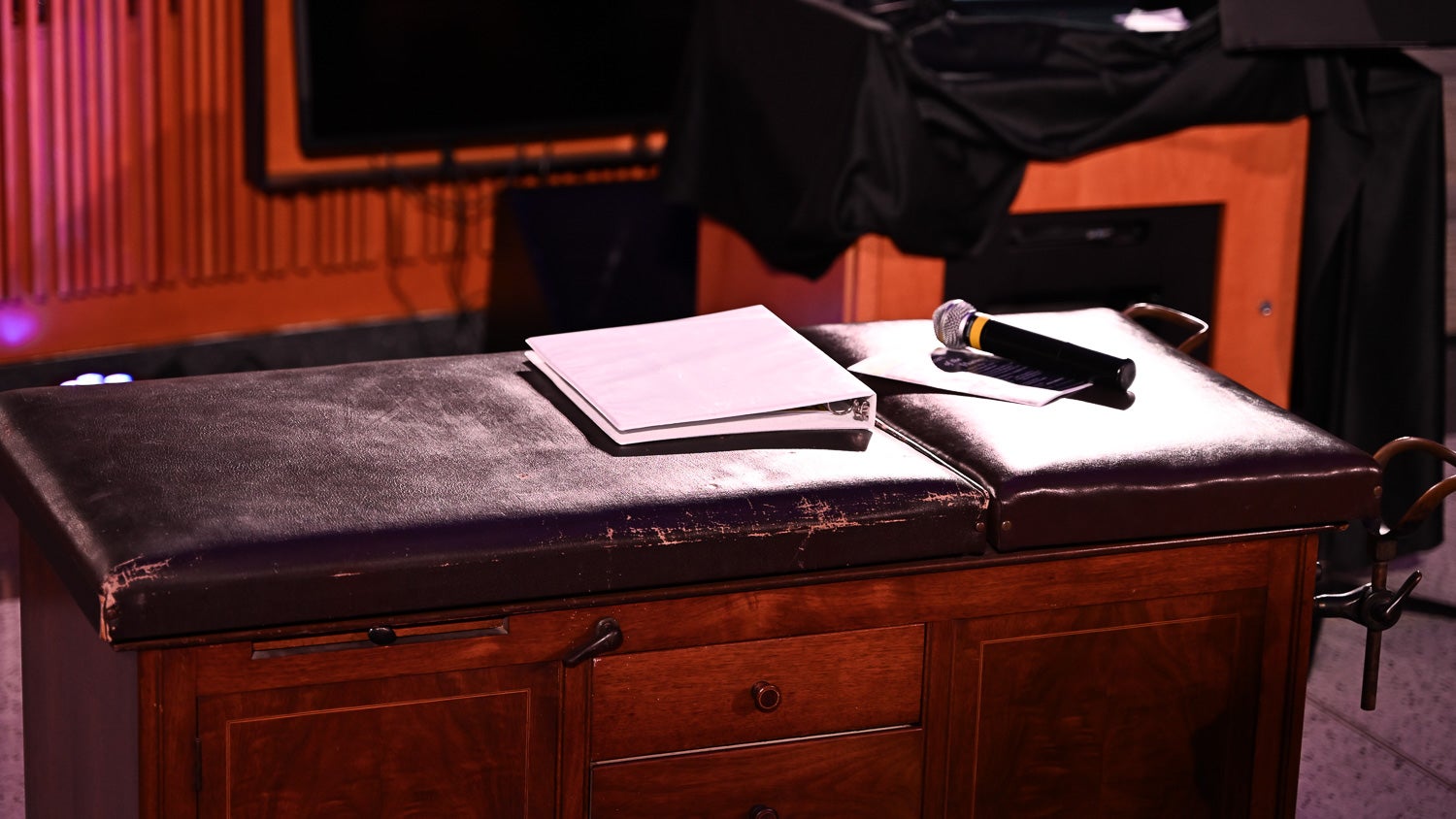 A microphone and binder of notes rest on the antique operating table on the Harvey Amphitheater stage
