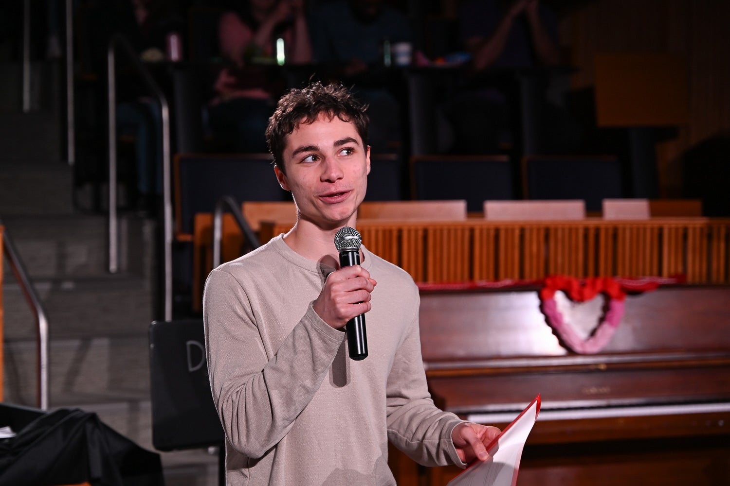 Undergraduate student Ben Notaris holds a microphone and script while performingUndergraduate student Raquel Silva dances on the Harvey Amphitheater stage