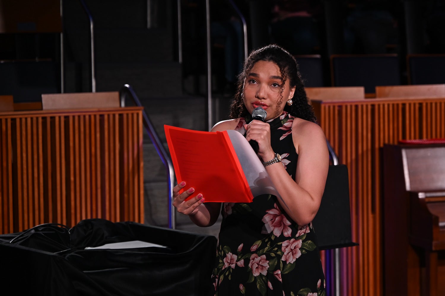 Master's student Alba Jeronimo holds a microphone and folder while reciting her poem