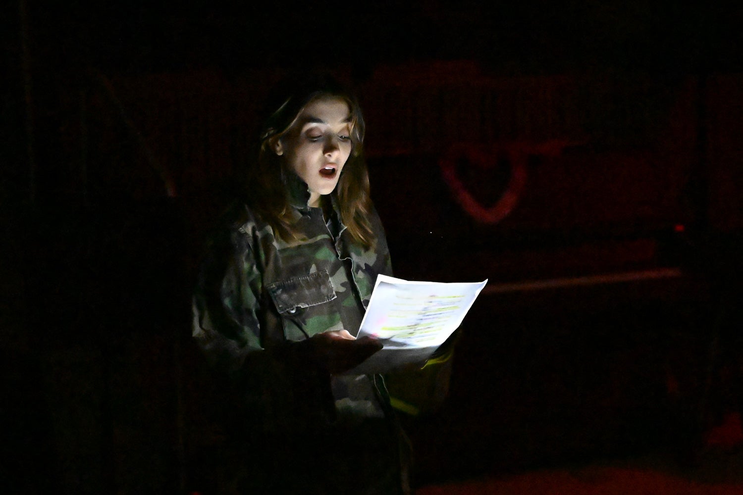 Undergraduate student Sofi Fateh, wearing a camouflage jacket, reads her lines by flashlight on the darkened Harvey Amphitheater stage