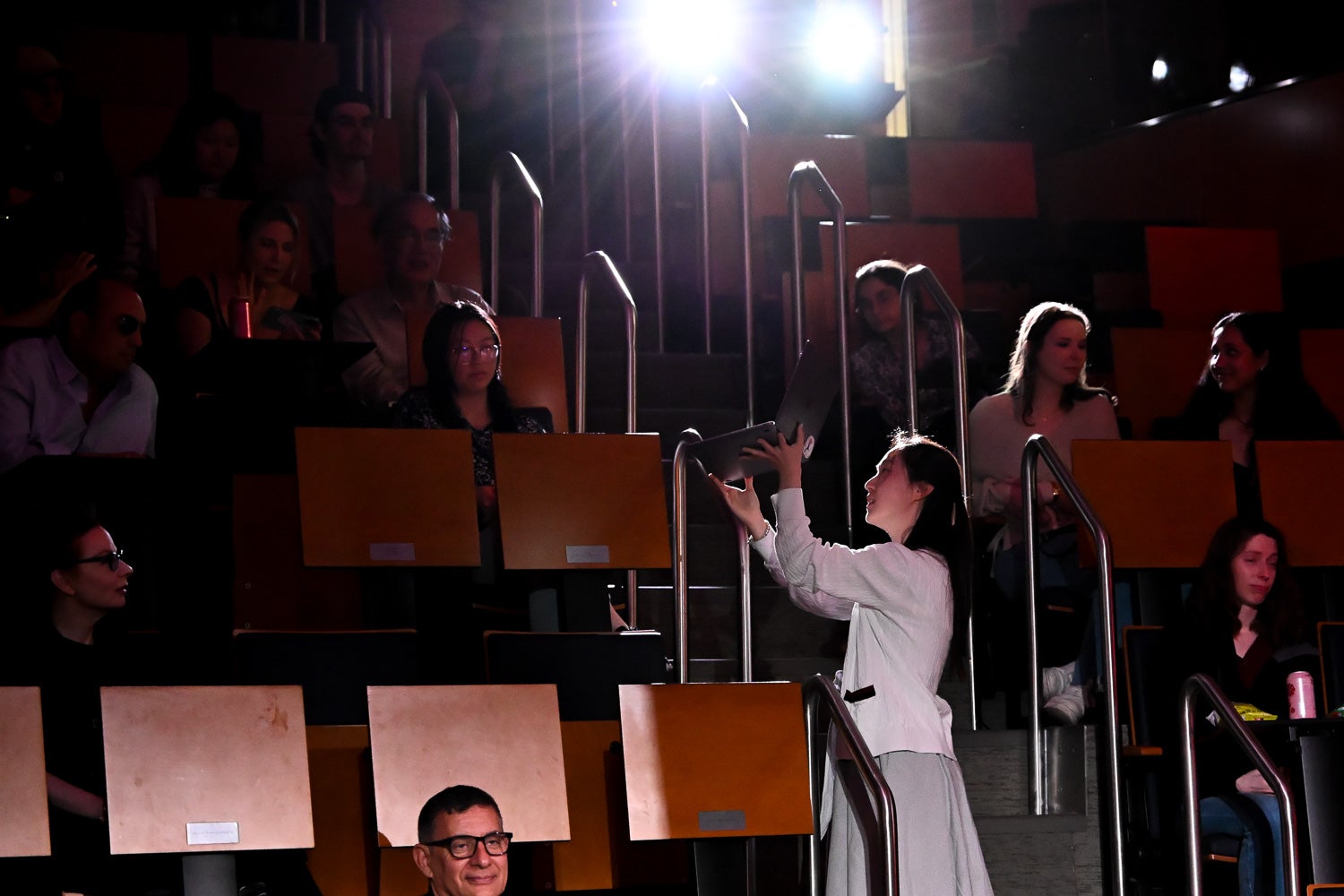 Medical student Stella SeoHyeon Lee stands amid the seating tiers in Harvey Amphitheater, holding up a laptop playing her choreographed ice skating routine