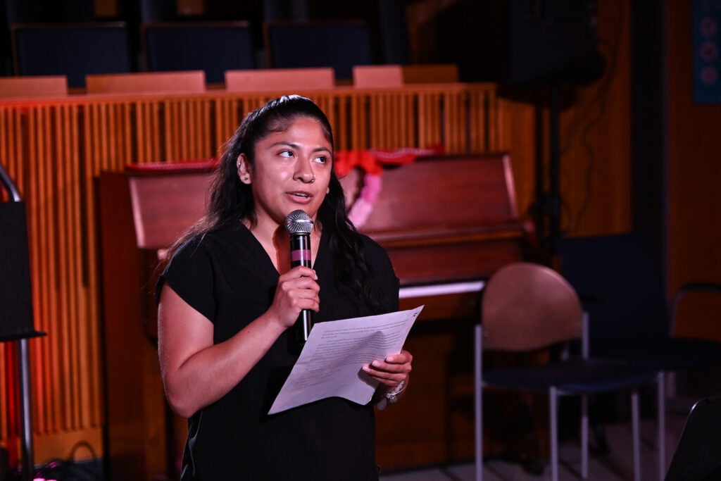 Integrative Medicine & Health Sciences master's student Shannon Miranda holds a microphone and paper while reciting "The Knowledge You Left Behind" on the Harvey Amphitheater stage