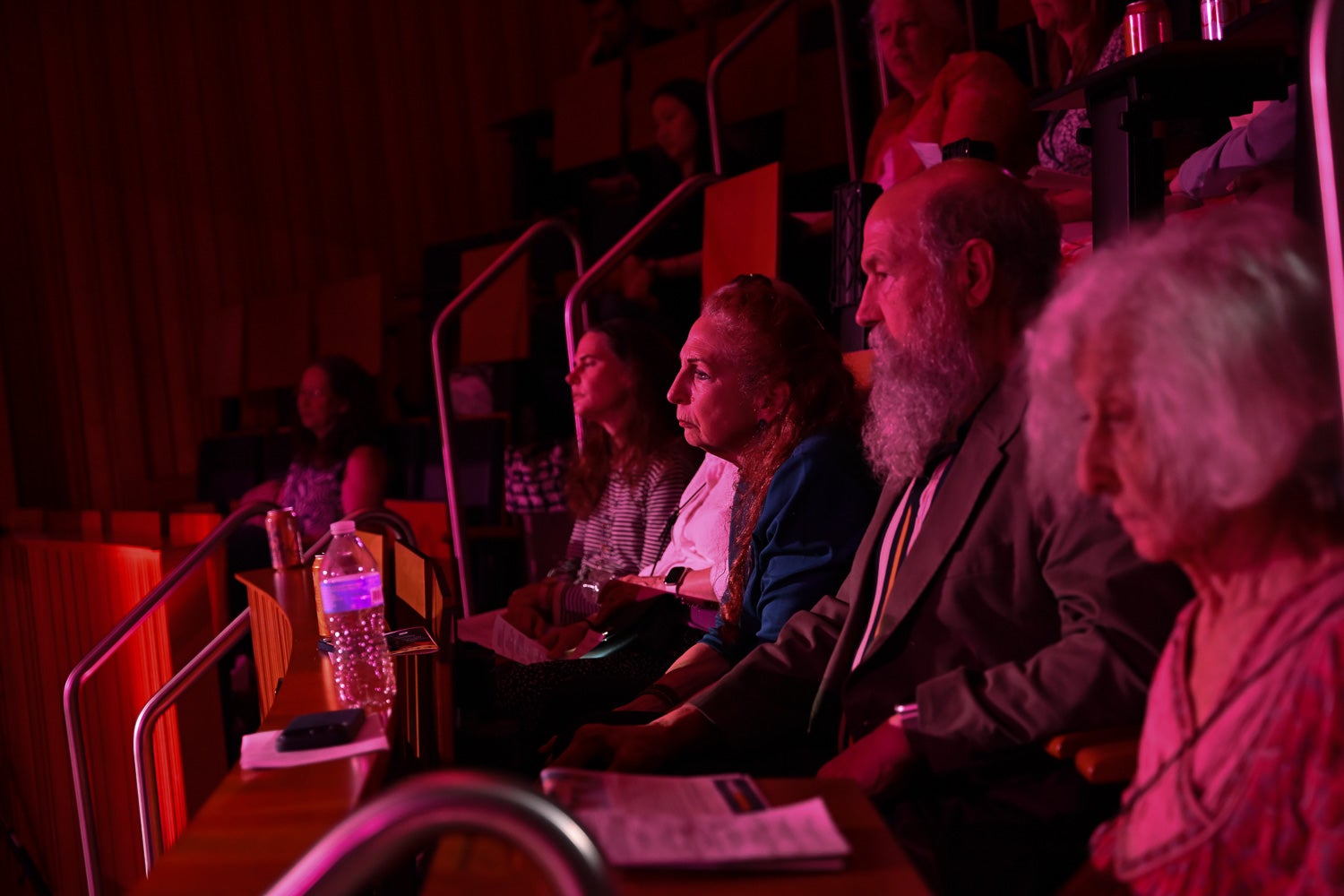 Audience members sit in the tiered seats of Harvey Amphitheater under pink stage lighting