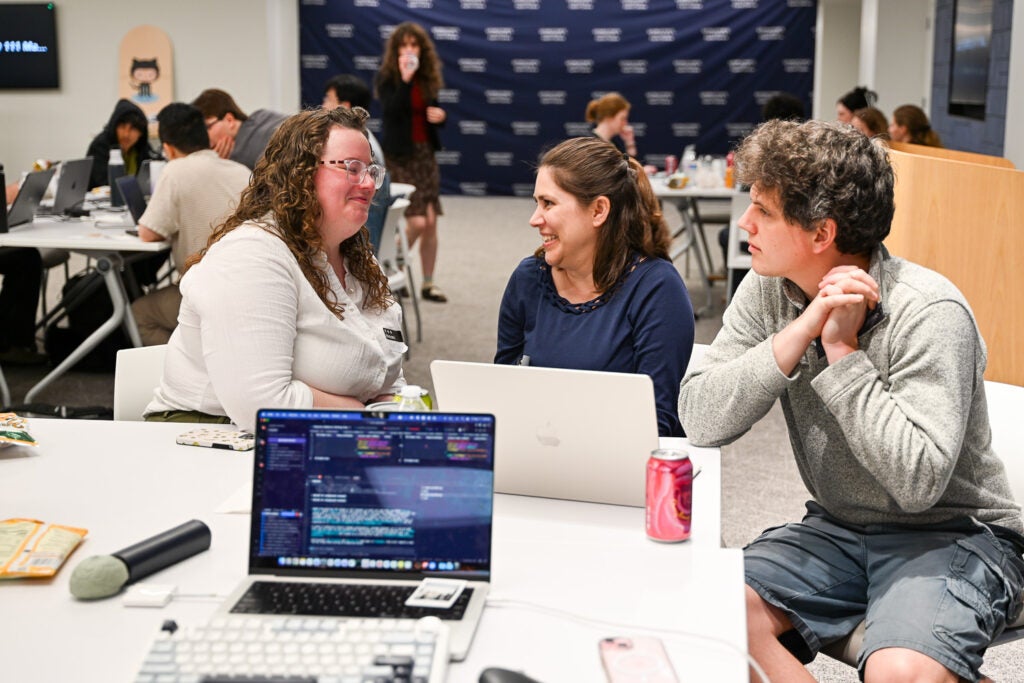 Three people talking seated at a table with laptops