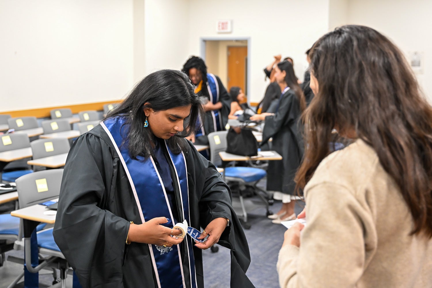 A graduate fixes her commencement regalia with tape in the line-up room