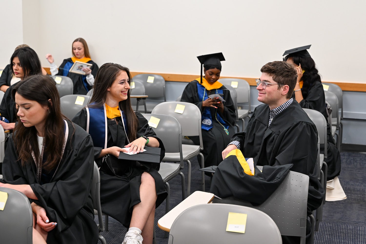 Graduates dressed in commencement regalia talk in the line-up room