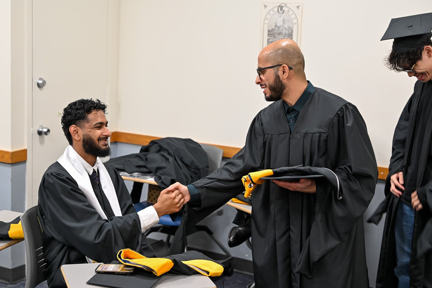 Graduates dressed in commencement regalia talk in the line-up room