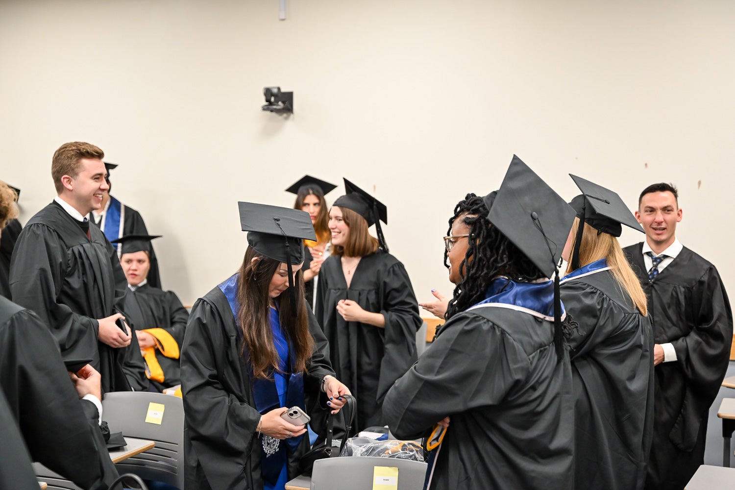 Graduates dressed in commencement regalia talk in the line-up room