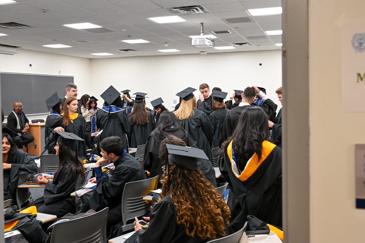 Graduates dressed in commencement regalia talk in the line-up room