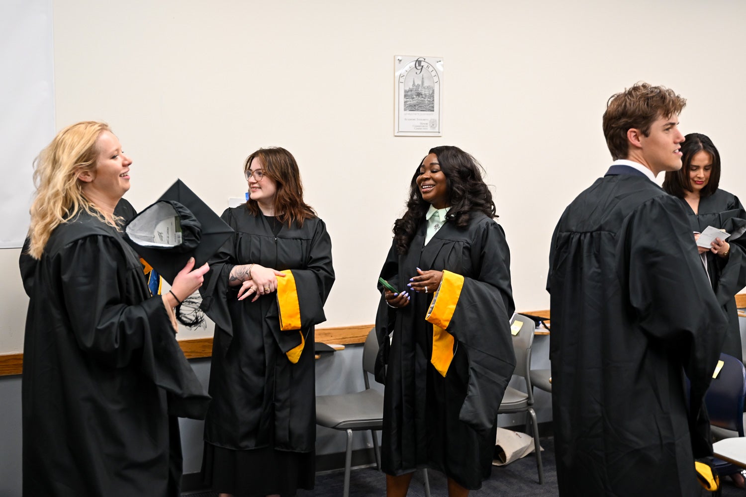 Graduates dressed in commencement regalia talk in the line-up room