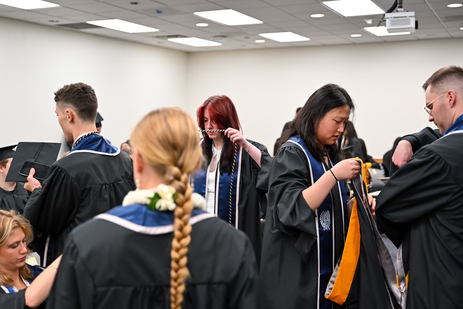 Graduates dressed in commencement regalia talk in the line-up room