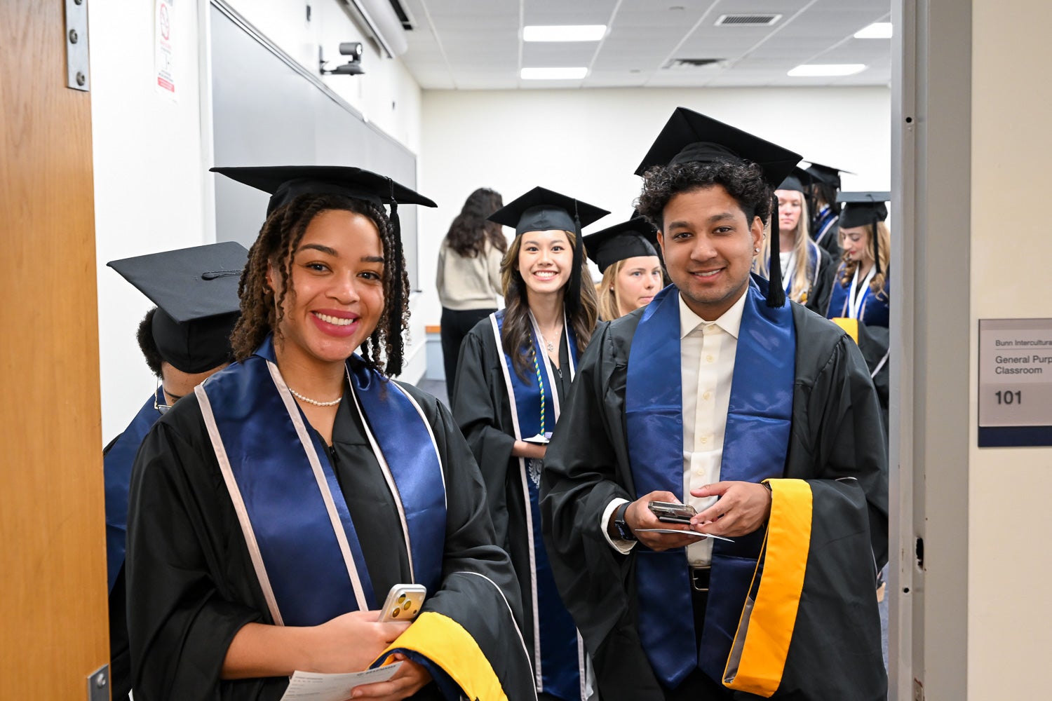 Graduates in their commencement regalia pose for a photo in a line-up room