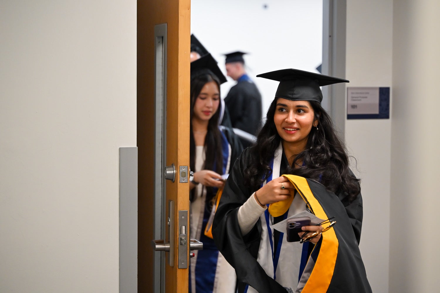 Graduates walk out of the line-up room in their commencement regalia