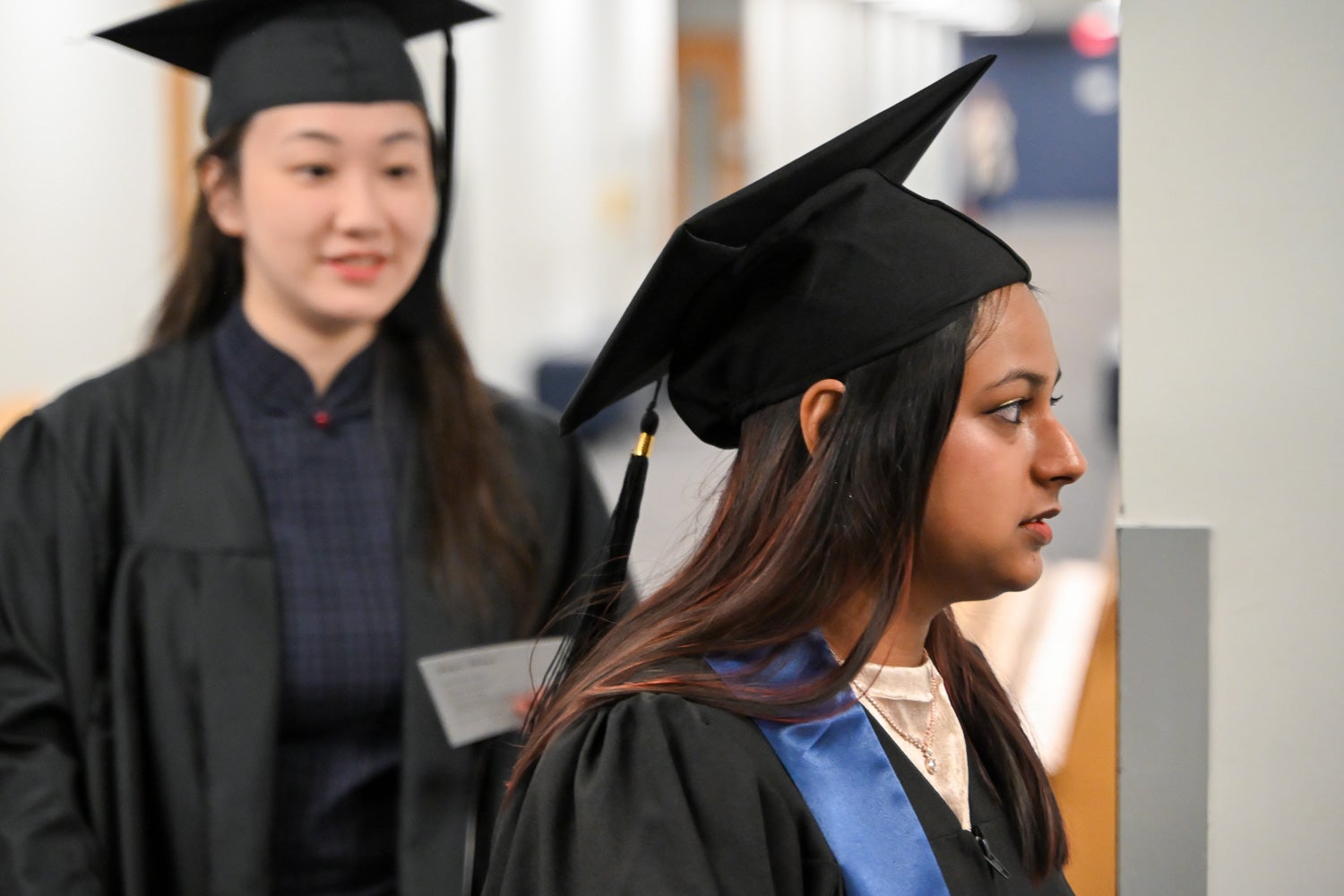 Graduates walk out of the line-up room in their commencement regalia