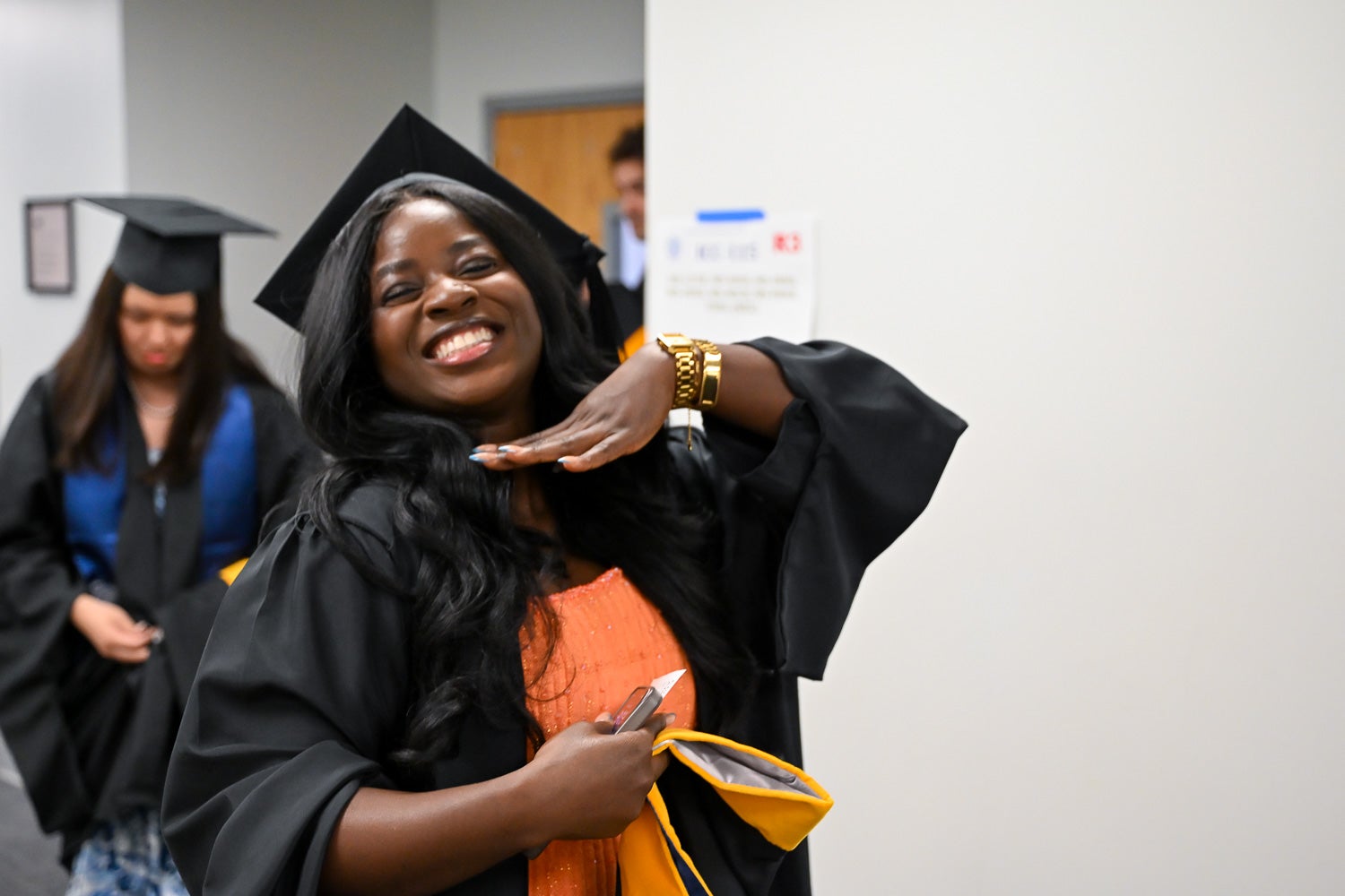 A graduate poses while walking out of the line-up room in commencement regalia