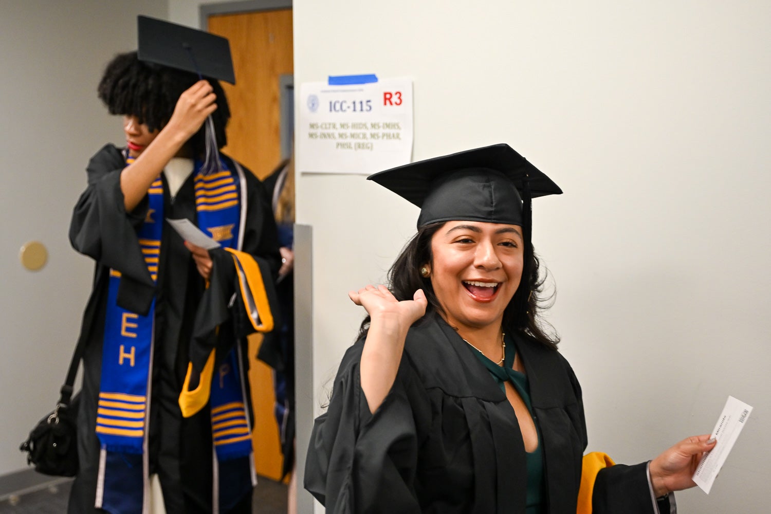 A graduate poses while walking out of the line-up room in commencement regalia