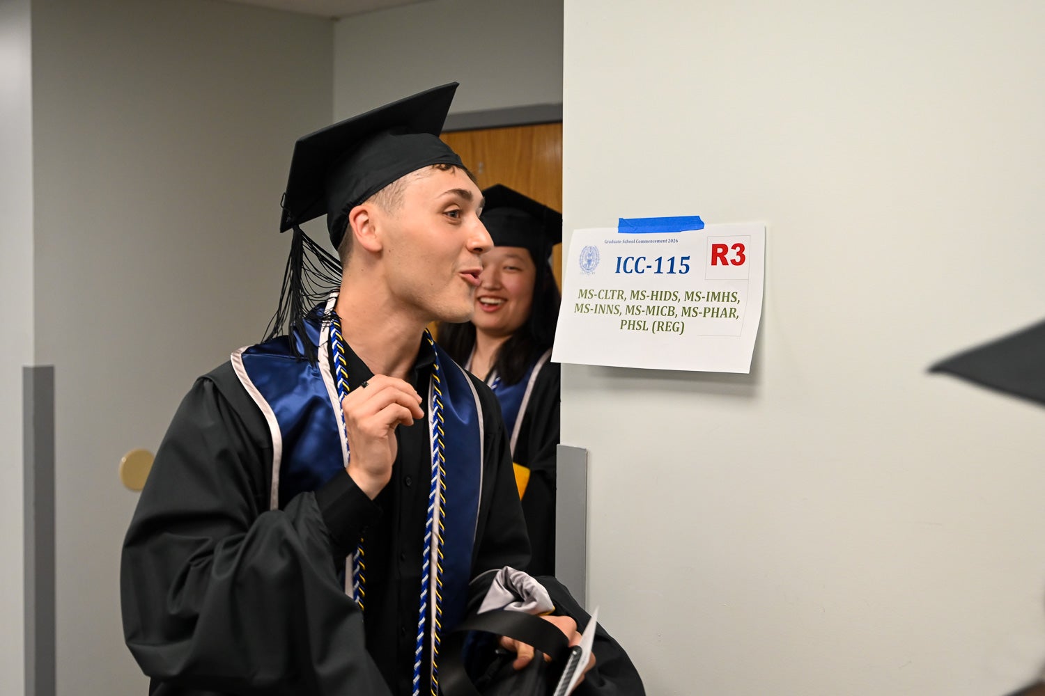 Graduates walk out of the line-up room in their commencement regalia