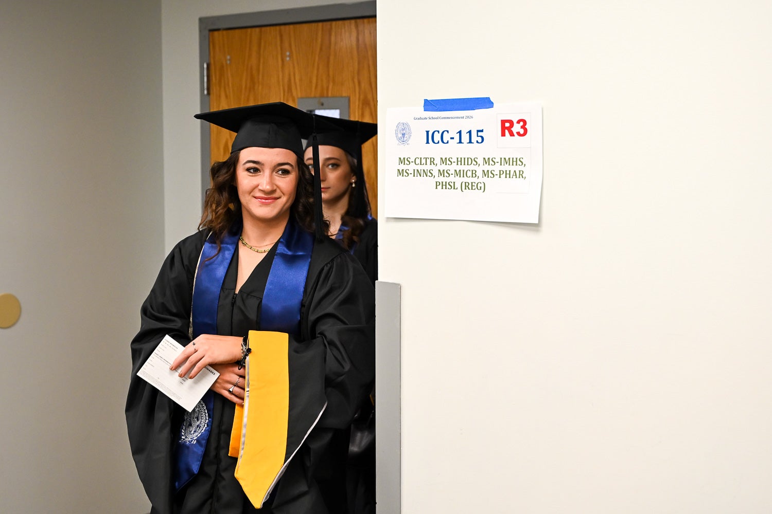 Graduates walk out of the line-up room in their commencement regalia