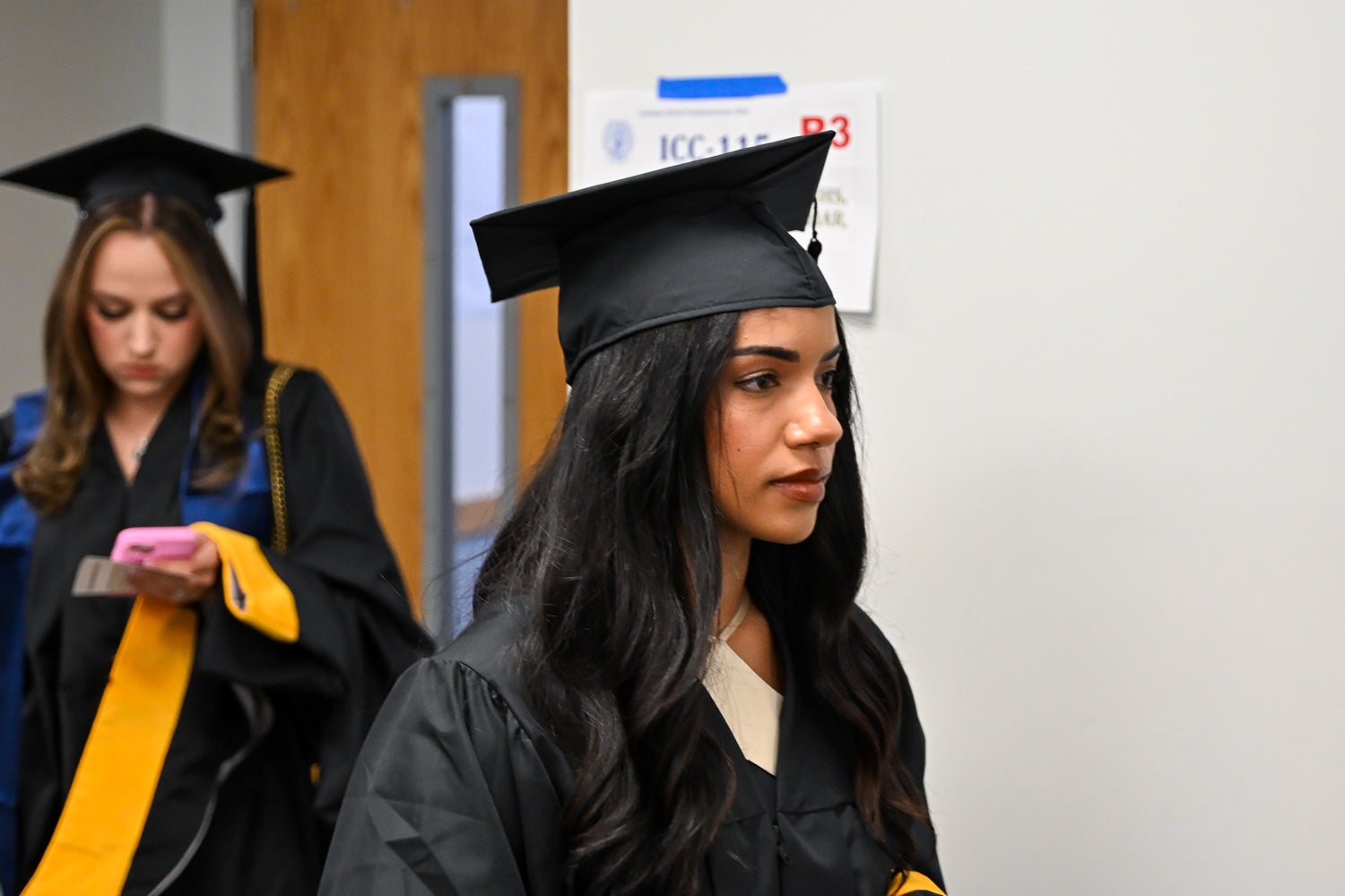 Graduates walk out of the line-up room in their commencement regalia