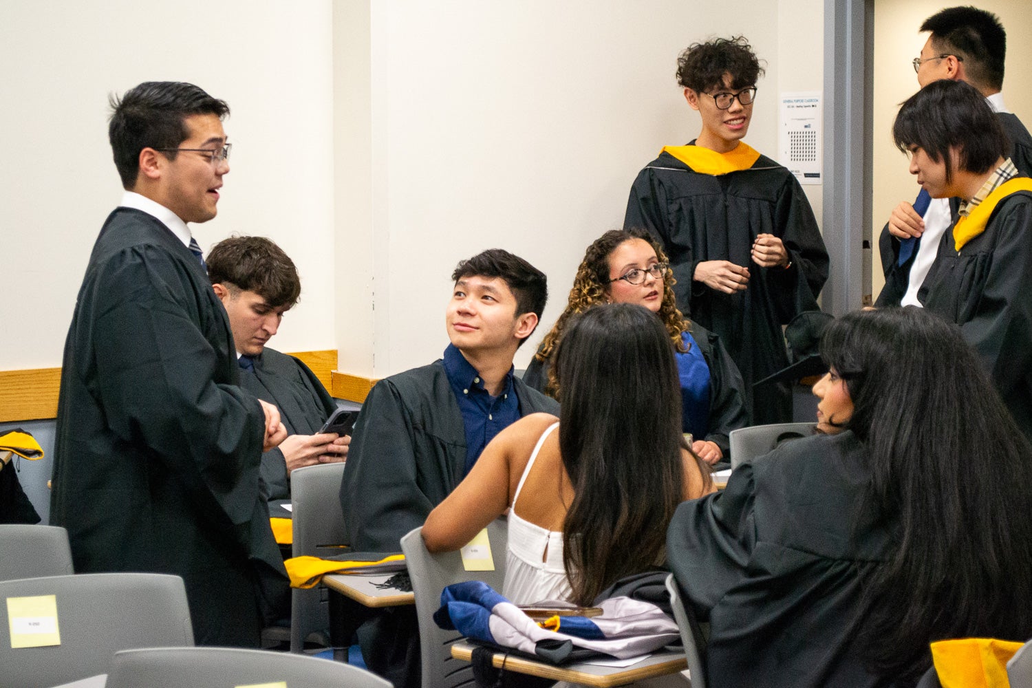 Graduates dressed in commencement regalia talk in the line-up room