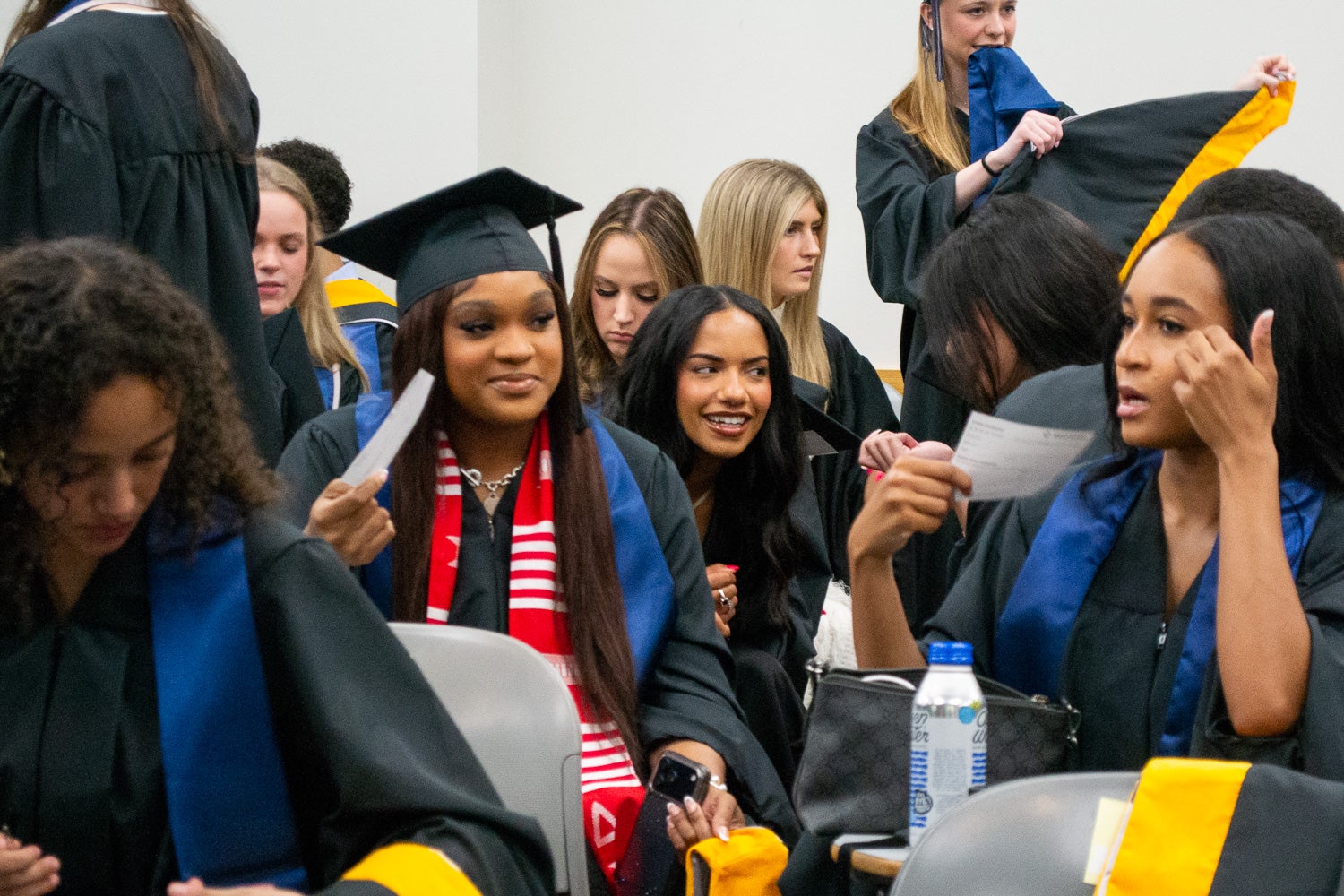 Graduates dressed in commencement regalia talk in the line-up room