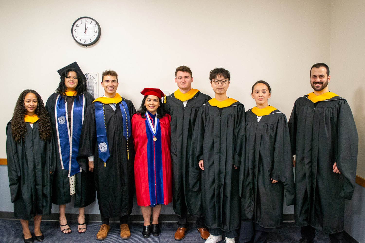 Graduates in their commencement regalia pose for a photo in a line-up room