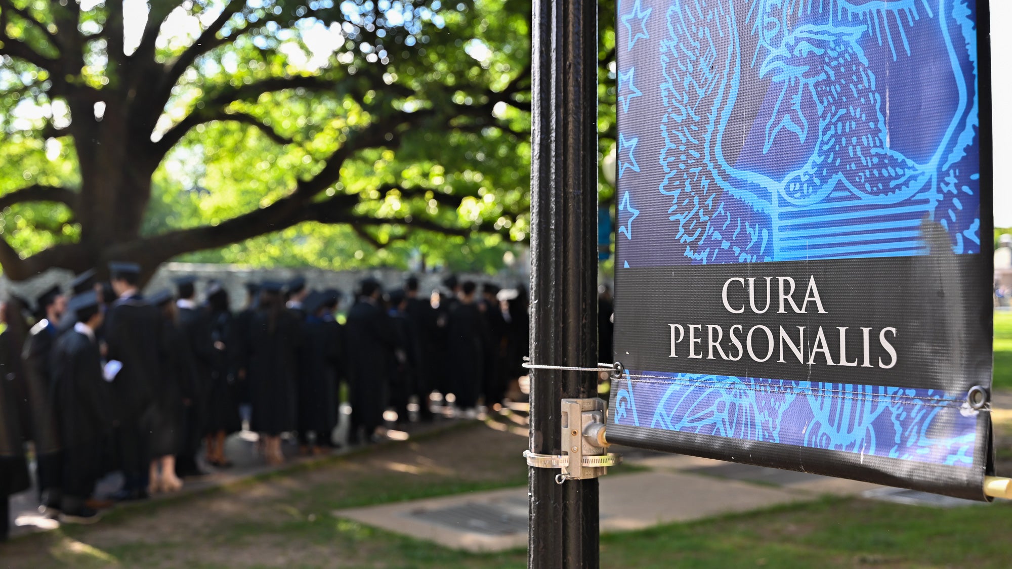 Graduates in commencement regalia process across Copley Lawn. In the foreground, a Georgetown 