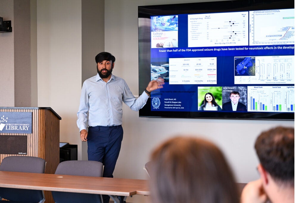 Pharmacology & Physiology Ph.D. student Anjik Ghosh gestures at his slide while presenting.