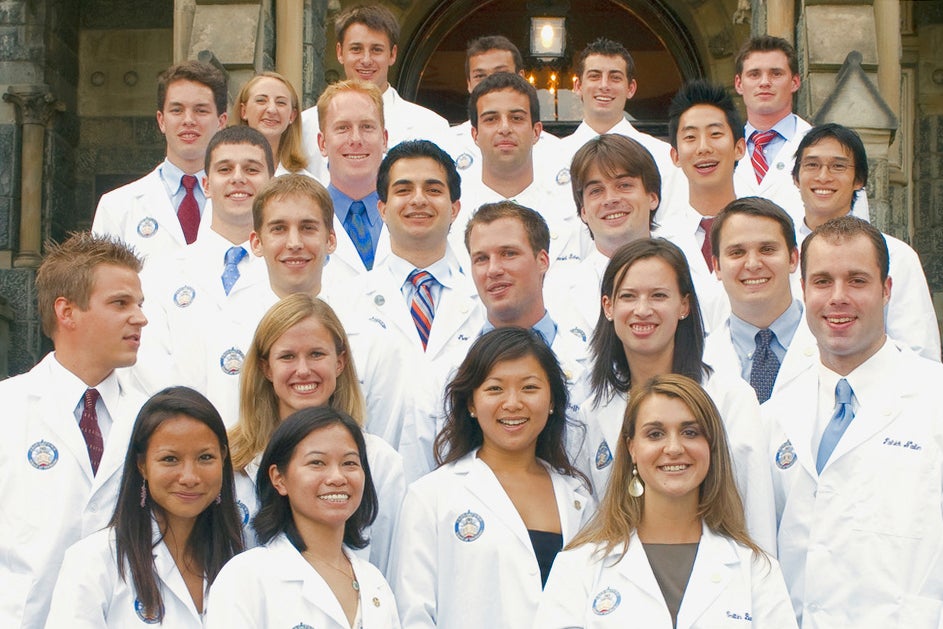 Students wearing white coats from the Georgetown University School of Medicine pose together on the steps of Healy Hall
