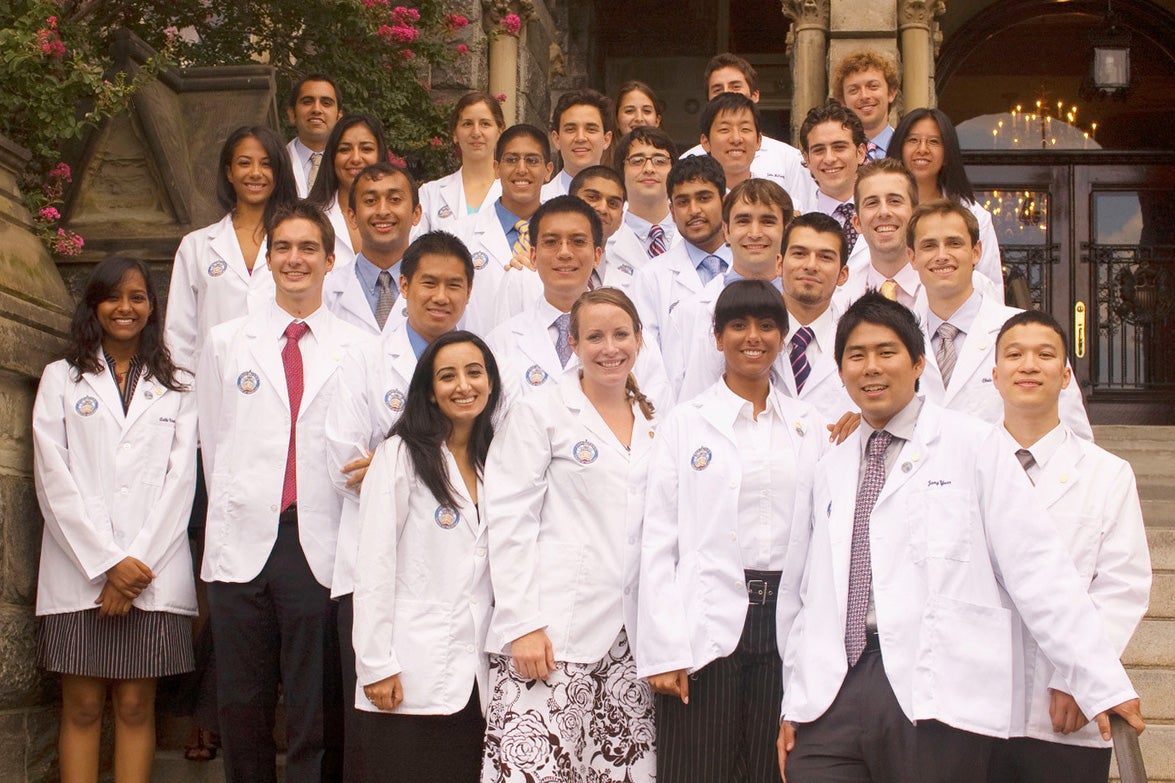 Students wearing white coats from the Georgetown University School of Medicine pose together on the steps of Healy Hall
