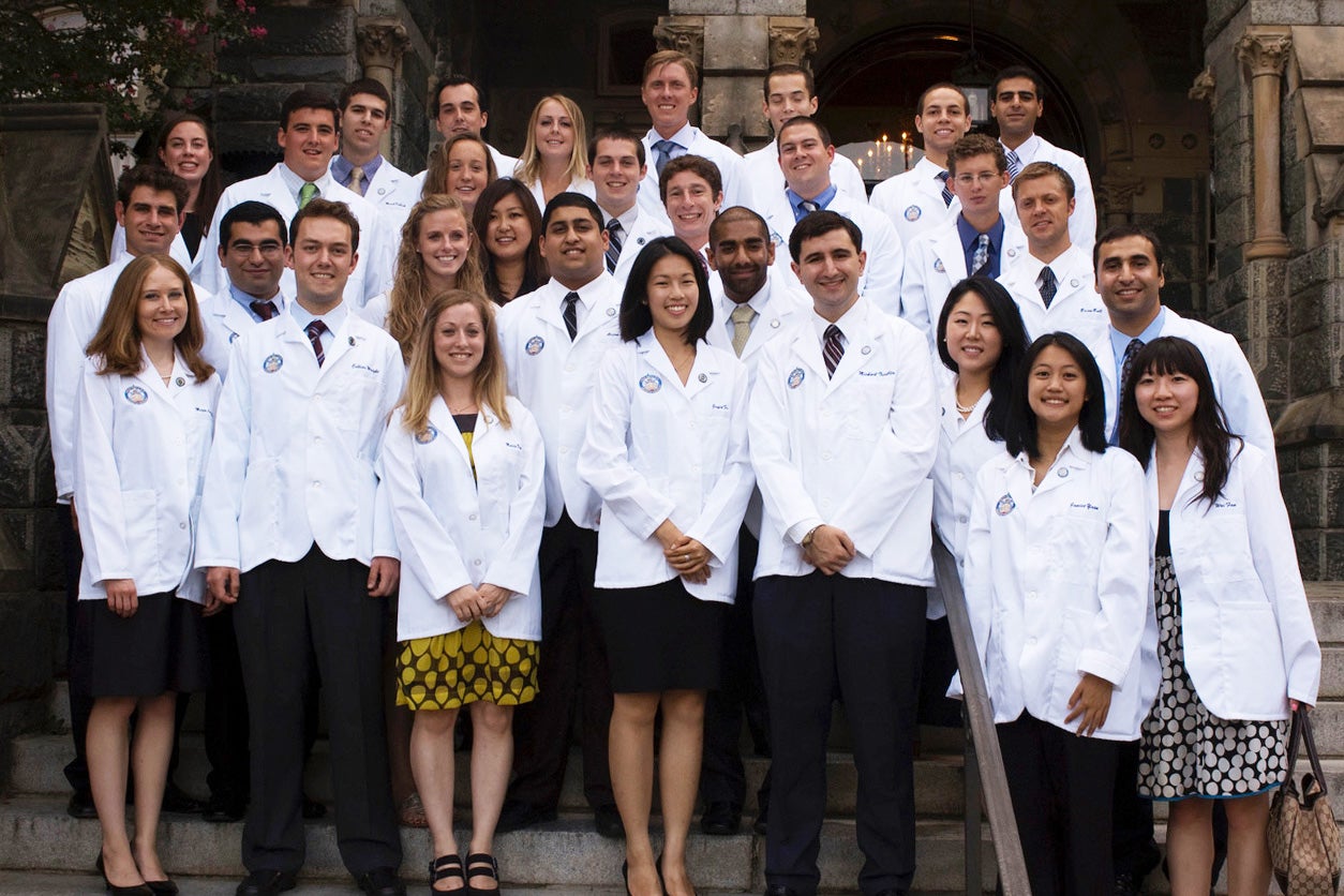 Students wearing white coats from the Georgetown University School of Medicine pose together on the steps of Healy Hall