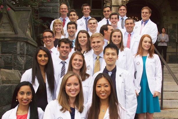 Students wearing white coats from the Georgetown University School of Medicine pose together on the steps of Healy Hall