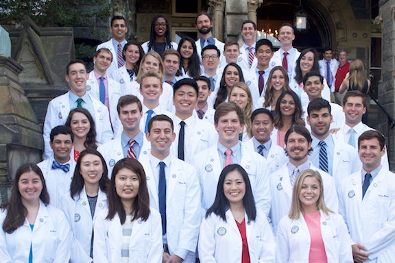 Students wearing white coats from the Georgetown University School of Medicine pose together on the steps of Healy Hall