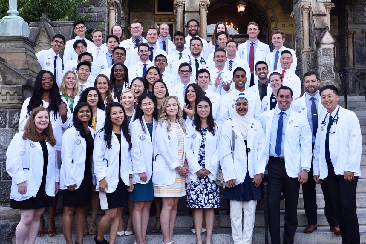 Students wearing white coats from the Georgetown University School of Medicine pose together on the steps of Healy Hall