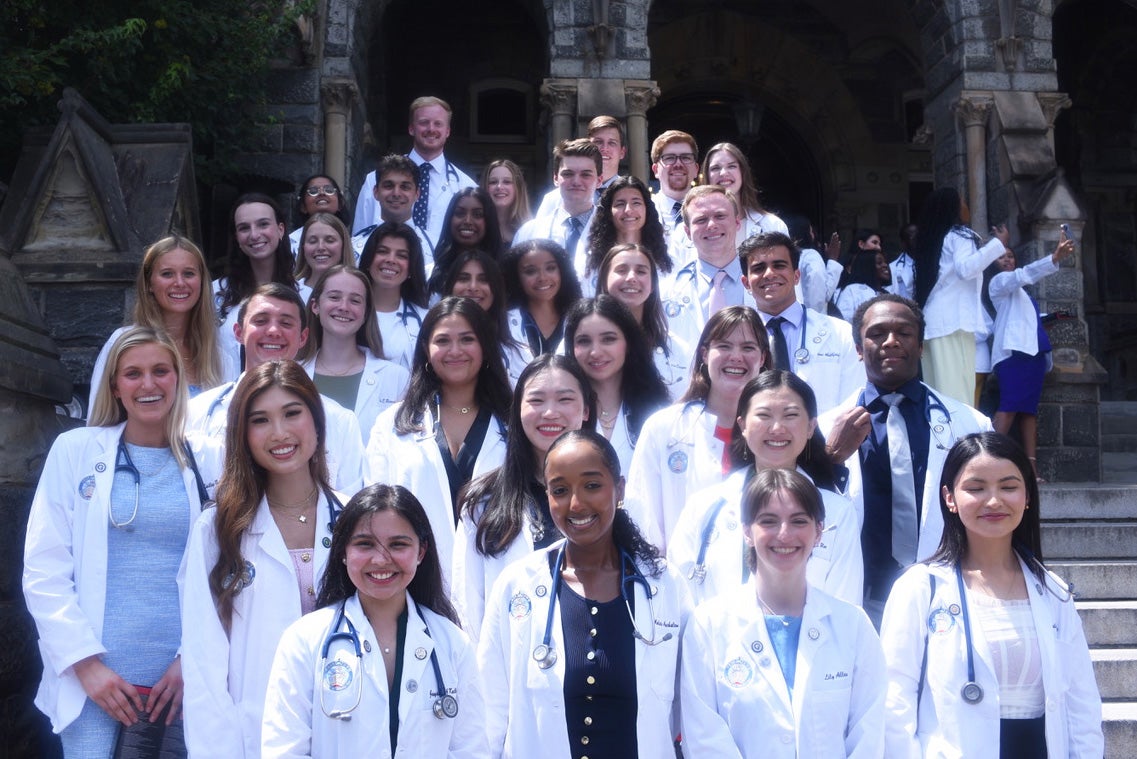 Students wearing white coats from the Georgetown University School of Medicine pose together on the steps of Healy Hall